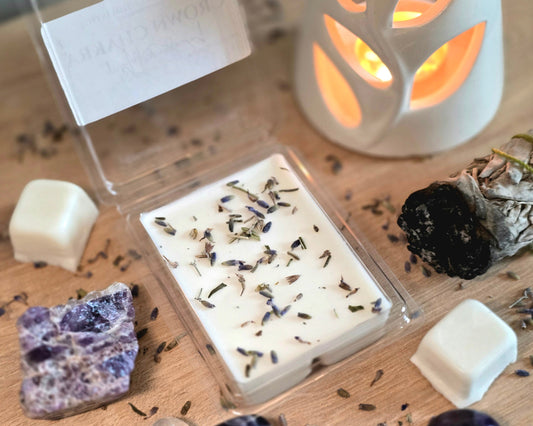 Crown Chakra Wax Melt with dried herbs in a clear container on a wooden surface with crystals, wax melt cubes, and a small wax melter.