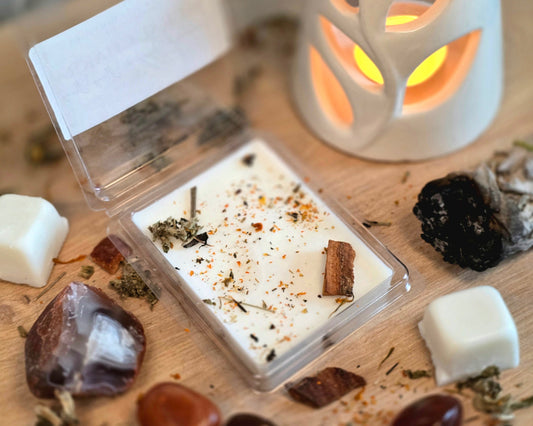Sacral Chakra Wax Melt with dried herbs in a clear container on a wooden surface with crystals, wax melt cubes, and a small wax melter.