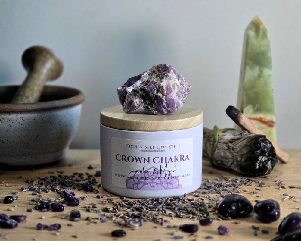 Crown Chakra Candle with a raw Amethyst Crystal on top of the lid, surrounded by crystals and herbs on a wooden surface.