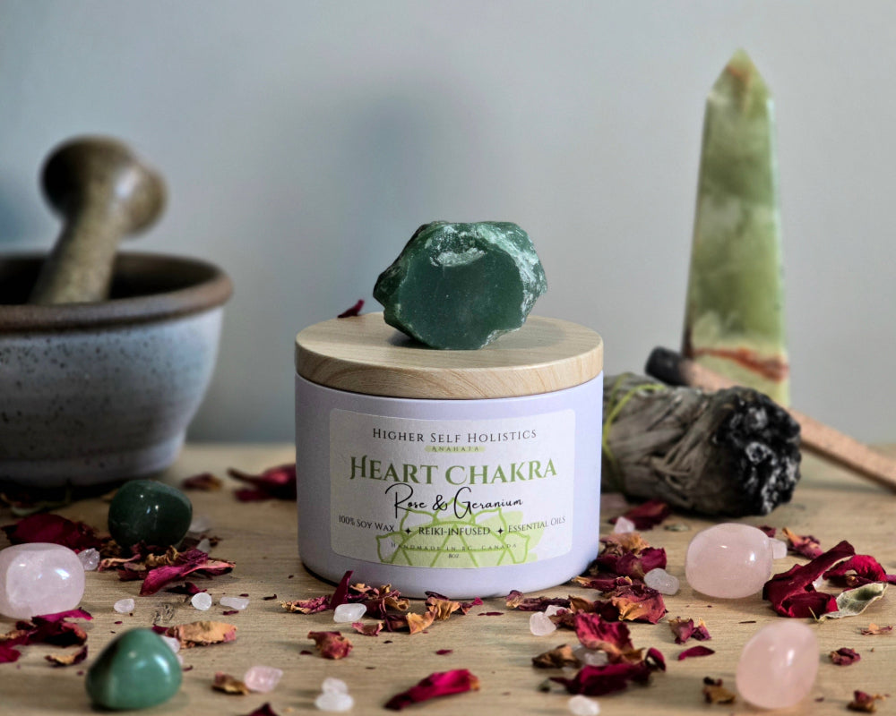 Heart Chakra Candle with a raw Green Aventurine Crystal on top of the lid, surrounded by crystals and herbs on a wooden surface.