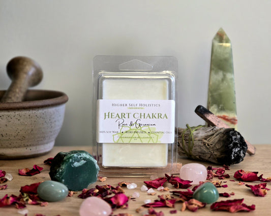 Heart Chakra Wax Melt in a clear container on a wooden surface with crystals, dried herbs,  smudge bundles, and a small mortar & pestle.