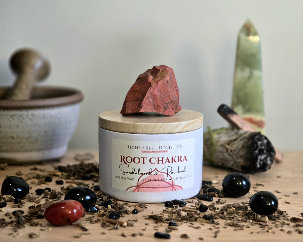 Root Chakra Candle with a raw Red Jasper Crystal on top of the lid, surrounded by crystals and herbs on a wooden surface.