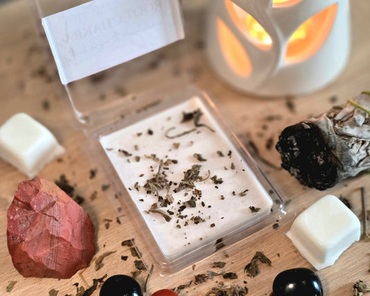 Root Chakra Wax Melt with dried herbs in a clear container on a wooden surface with crystals, wax melt cubes, and a small wax melter.