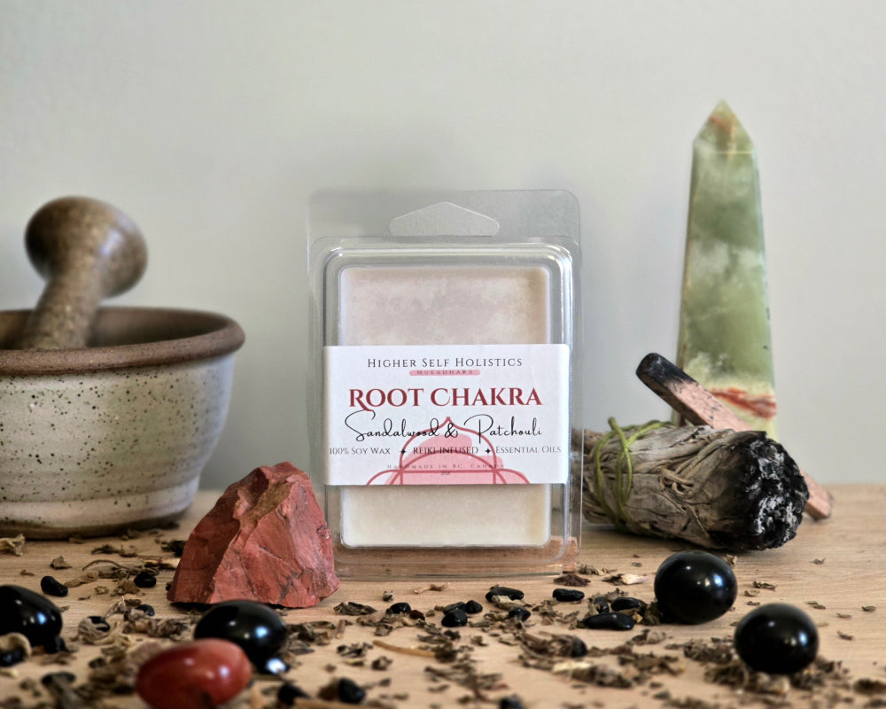 Root Chakra Wax Melt in a clear container on a wooden surface with crystals, dried herbs,  smudge bundles, and a small mortar & pestle.