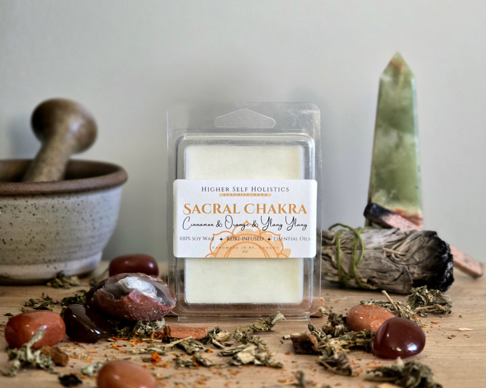 Sacral Chakra Wax Melt in a clear container on a wooden surface with crystals, dried herbs,  smudge bundles, and a small mortar & pestle.