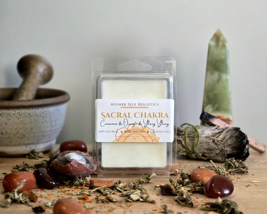 Sacral Chakra Wax Melt in a clear container on a wooden surface with crystals, dried herbs,  smudge bundles, and a small mortar & pestle.