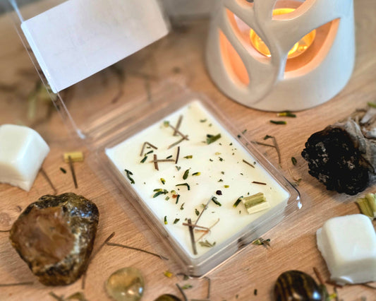 Solar Plexus Chakra Wax Melt with dried herbs in a clear container on a wooden surface with crystals, wax melt cubes, and a small wax melter.