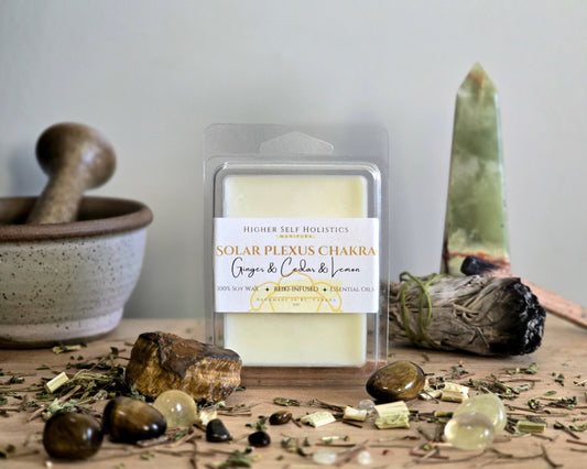 Solar Plexus Chakra Wax Melt in a clear container on a wooden surface with crystals, dried herbs,  smudge bundles, and a small mortar & pestle.