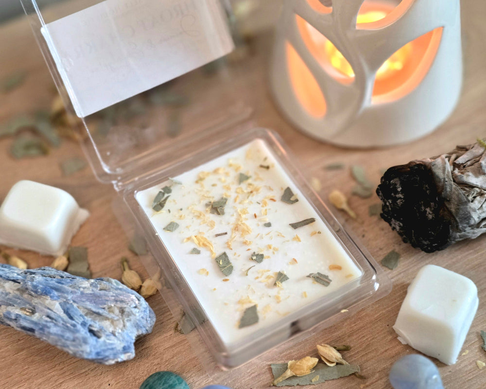 Throat Chakra Wax Melt with dried herbs in a clear container on a wooden surface with crystals, wax melt cubes, and a small wax melter.