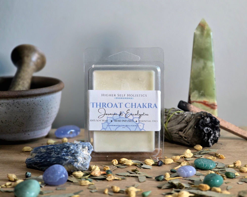 Throat Chakra Wax Melt in a clear container on a wooden surface with crystals, dried herbs,  smudge bundles, and a small mortar & pestle.