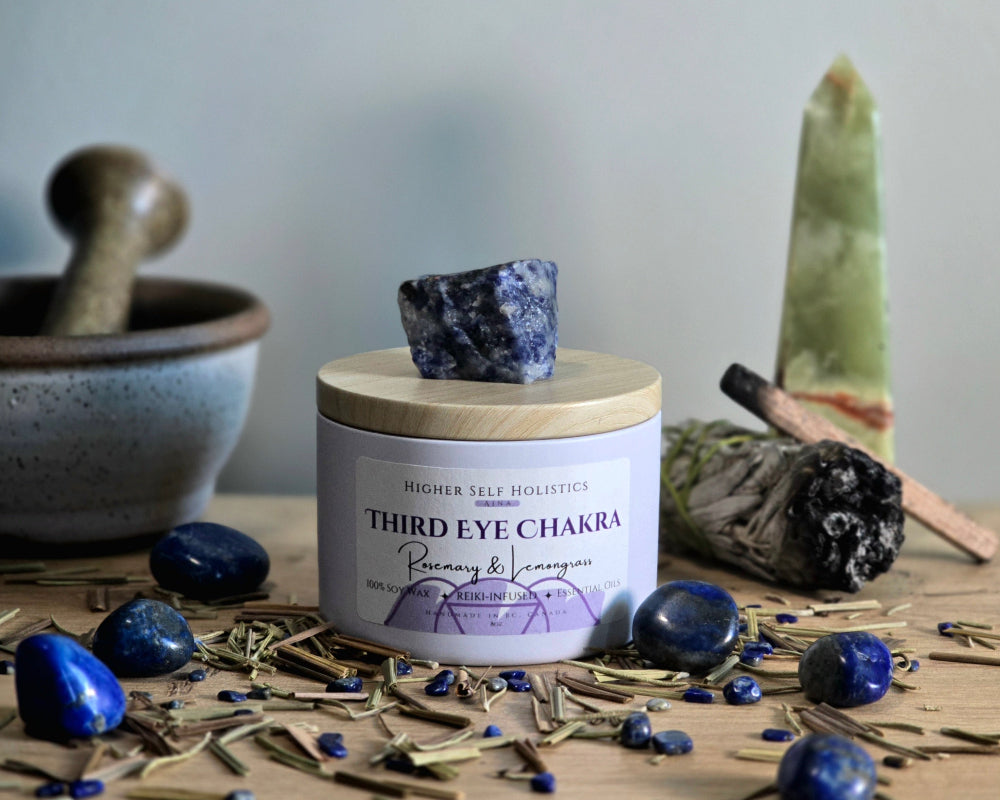 Third Eye Chakra Candle with a raw Lapis Lazuli Crystal on top of the lid, surrounded by crystals and herbs on a wooden surface.