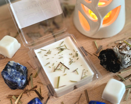 Third Eye Chakra Wax Melt with dried herbs in a clear container on a wooden surface with crystals, wax melt cubes, and a small wax melter.